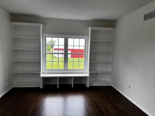 Room with window seat flanked by white bookshelves, dark wood floor.