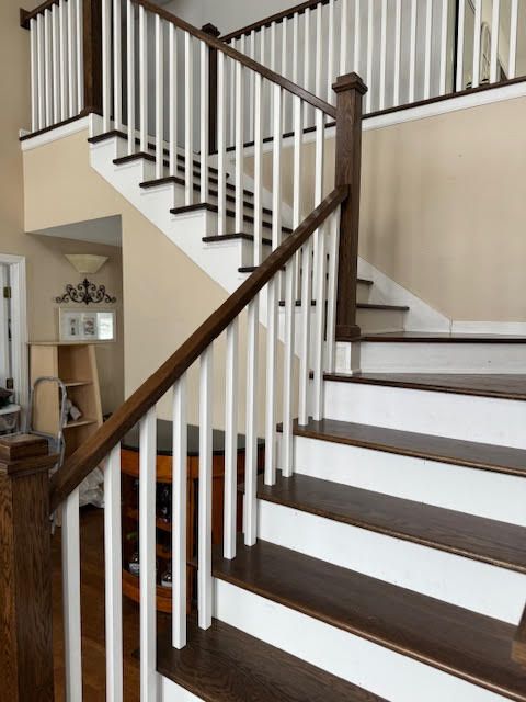 Wooden staircase with white spindles, dark wood steps, and brown handrails. Interior setting.