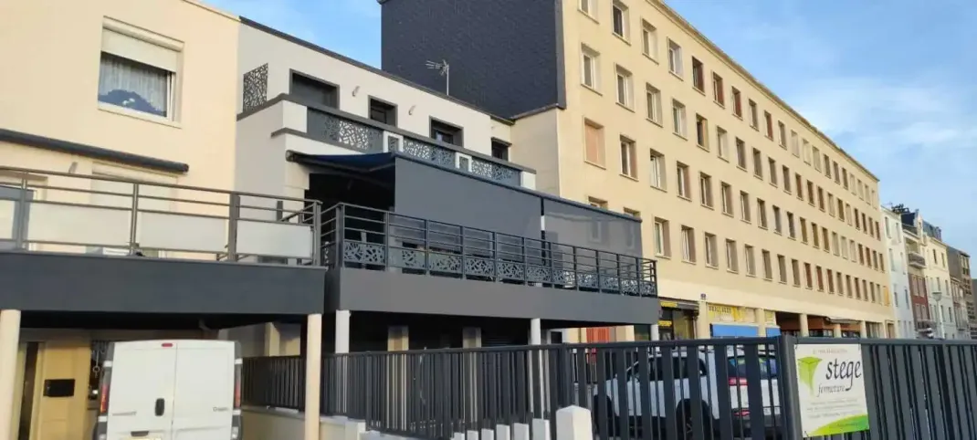 Un grand bâtiment entouré d'une clôture et une camionnette blanche garée devant.