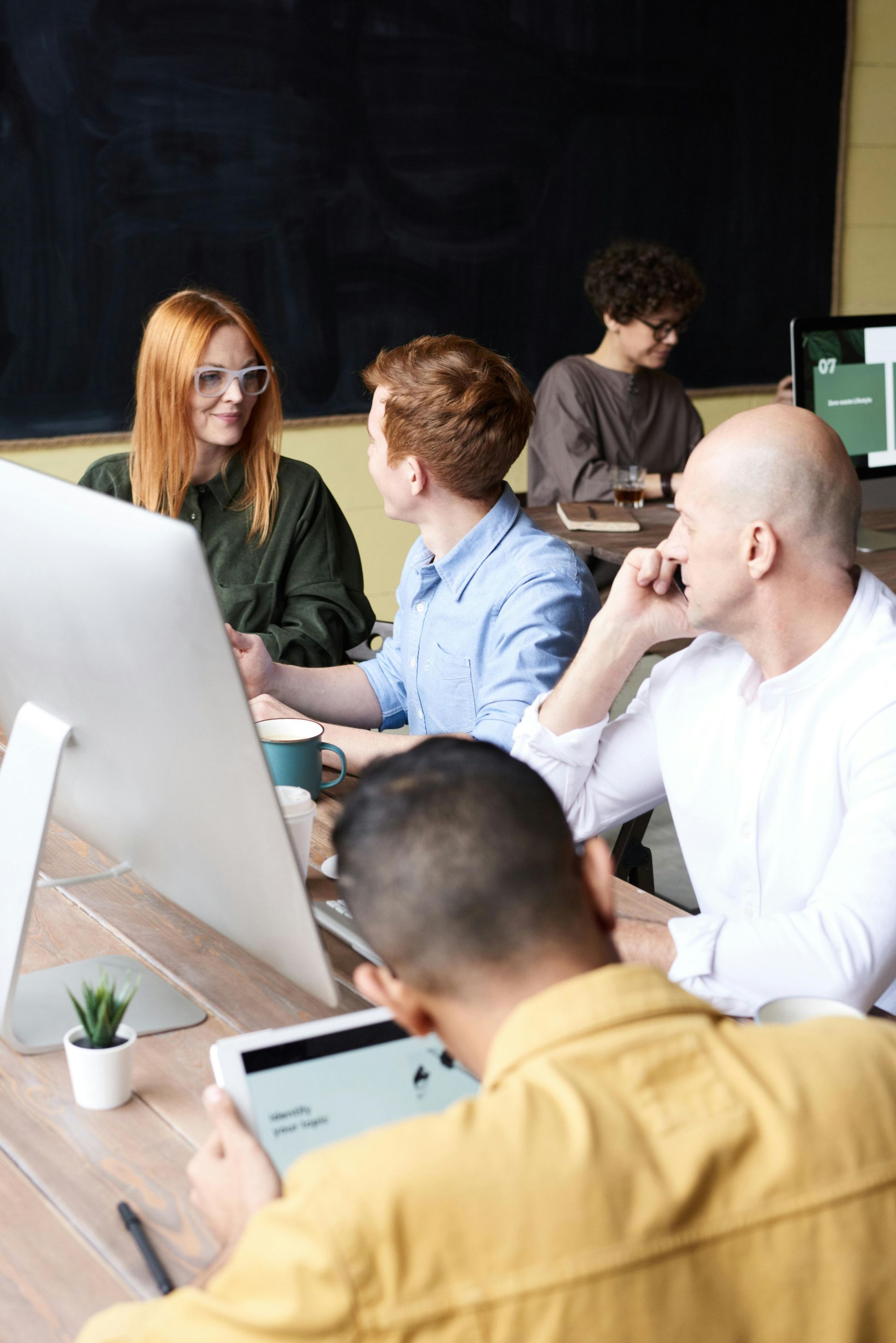 People collaborating around computers and tablet in a brightly lit office setting.