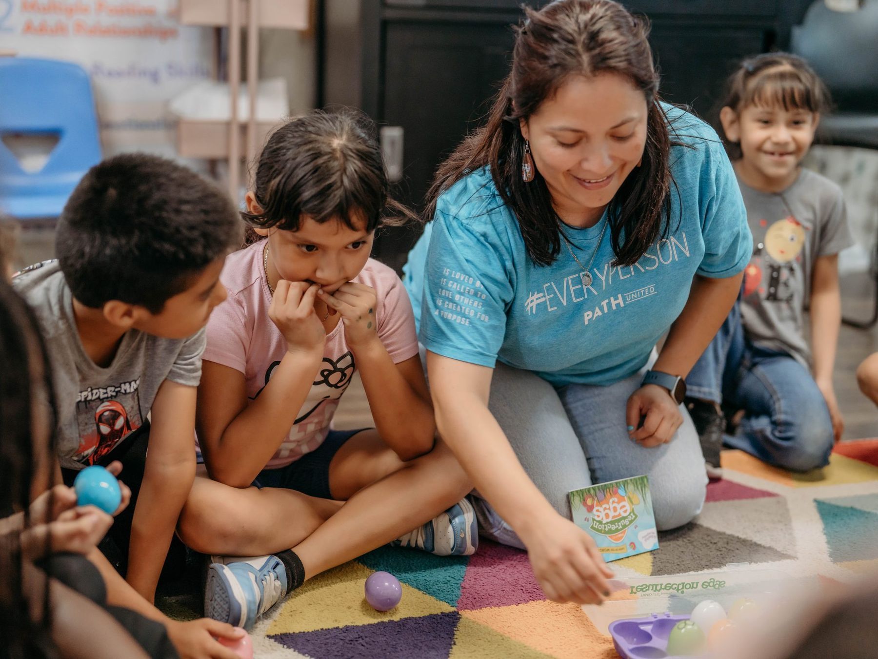 A Path United teacher sitting on the floor with students leaning in to a lesson