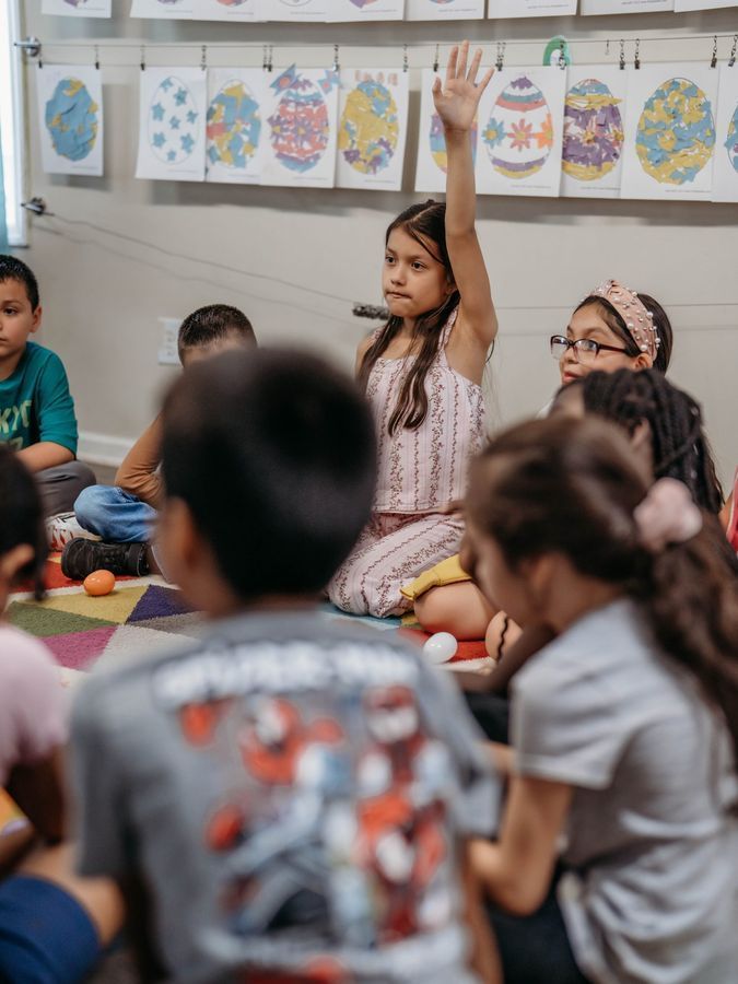 A student raising her hand during a lesson on the classroom rug