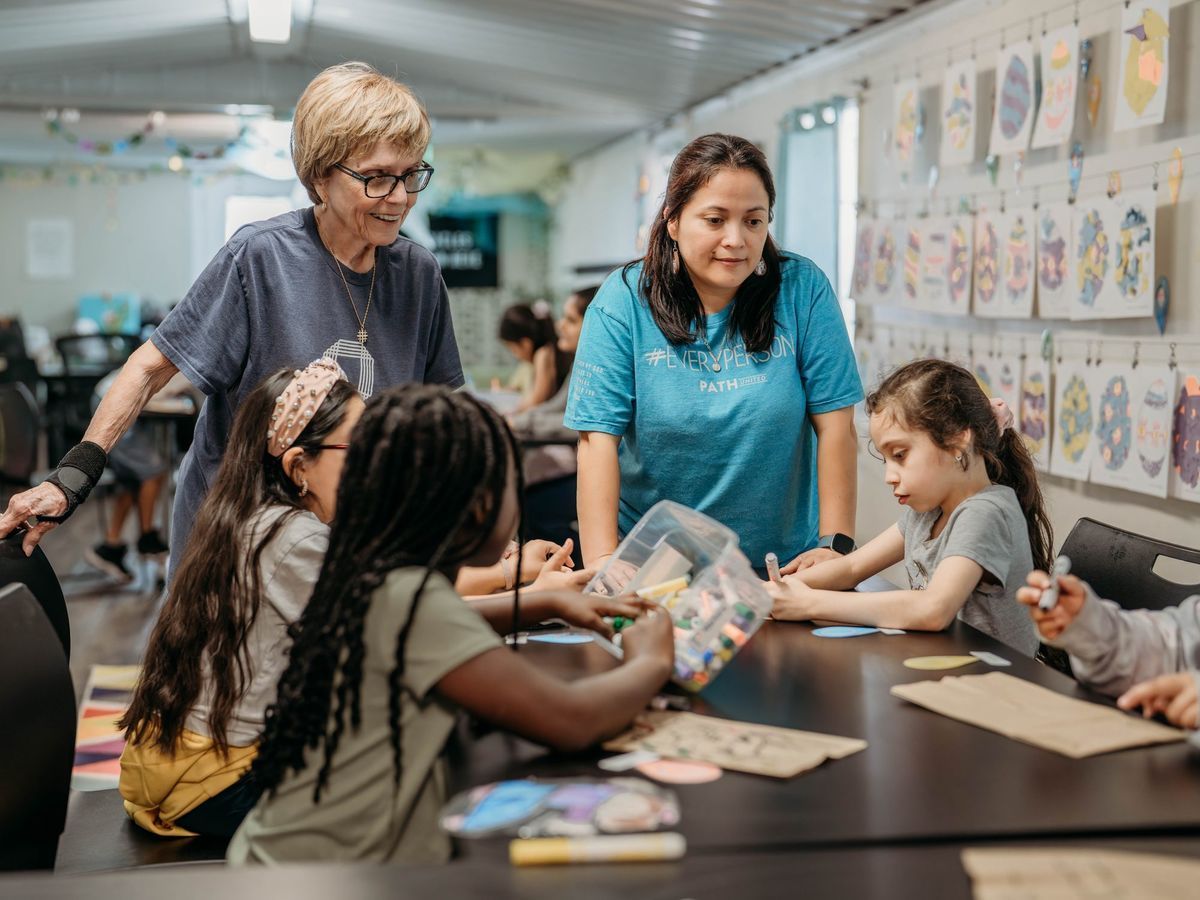 A volunteer and a teacher working alongside kids at a craft table