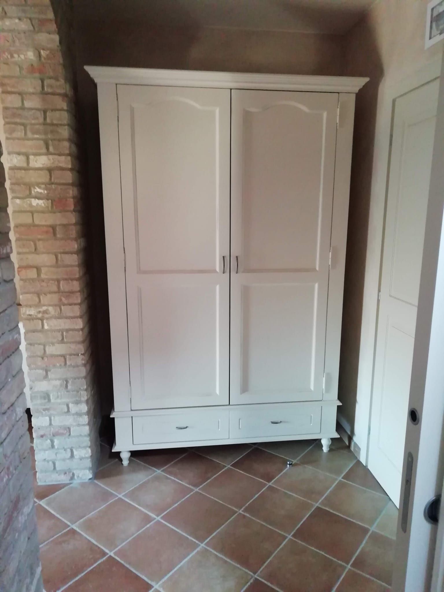 Un armadio bianco è appoggiato su un pavimento piastrellato accanto a un muro di mattoni