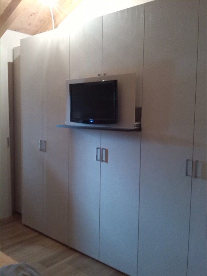 Una camera da letto con armadi bianchi e una tv a schermo piatto appesa al muro.