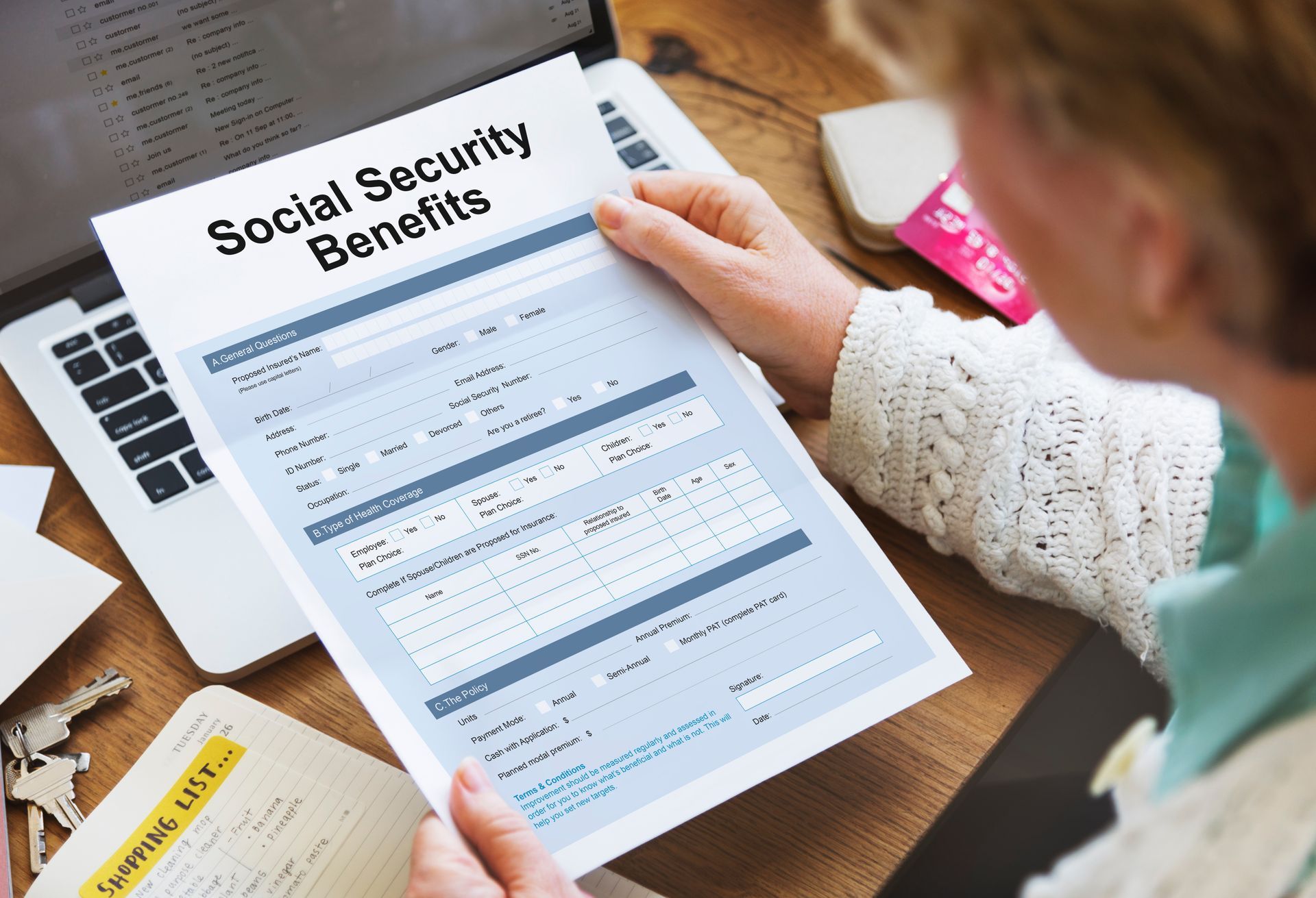 Person holding a Social Security Benefits form near a laptop.