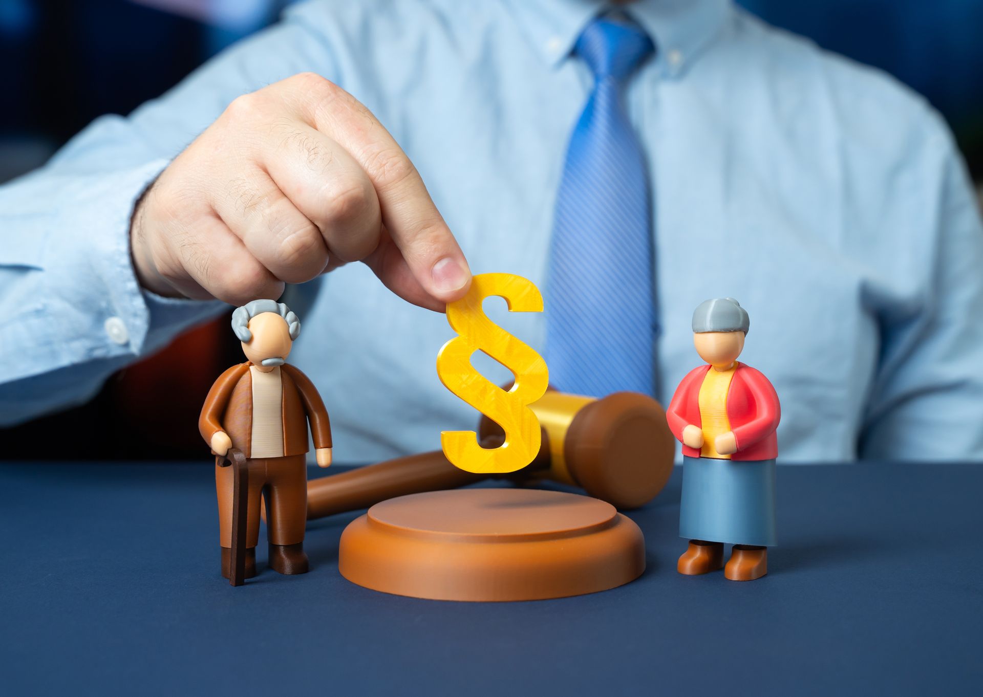 Hand placing a gold dollar sign beside a gavel and two figurines on a blue desk