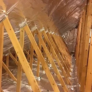 Attic with rows of yellow wooden braces under a reflective insulated roof