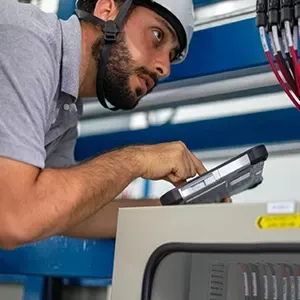 Technician in gray shirt using a tablet beside industrial equipment in a workshop