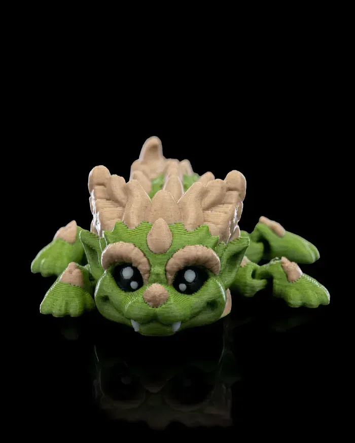 A green and brown toy dragon is laying on its back on a black surface.