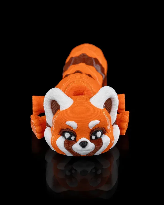 A 3d printed red panda is laying down on a black surface.