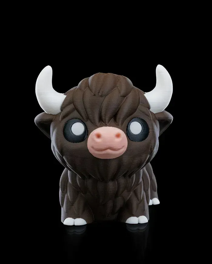 A brown bull with white horns and a pink nose is sitting on a black surface.