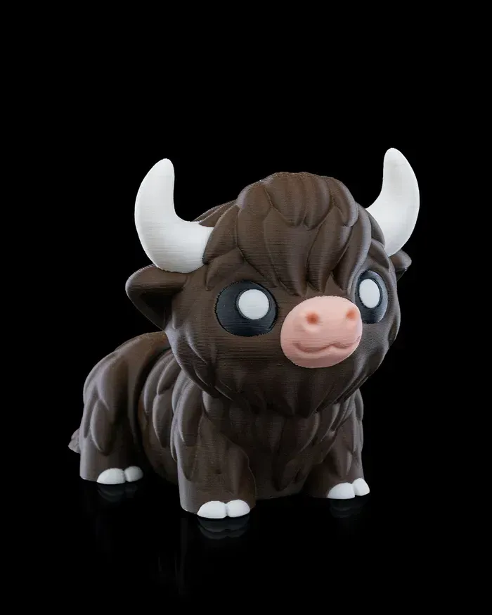 A brown bull with white horns and a pink nose is sitting on a black surface.