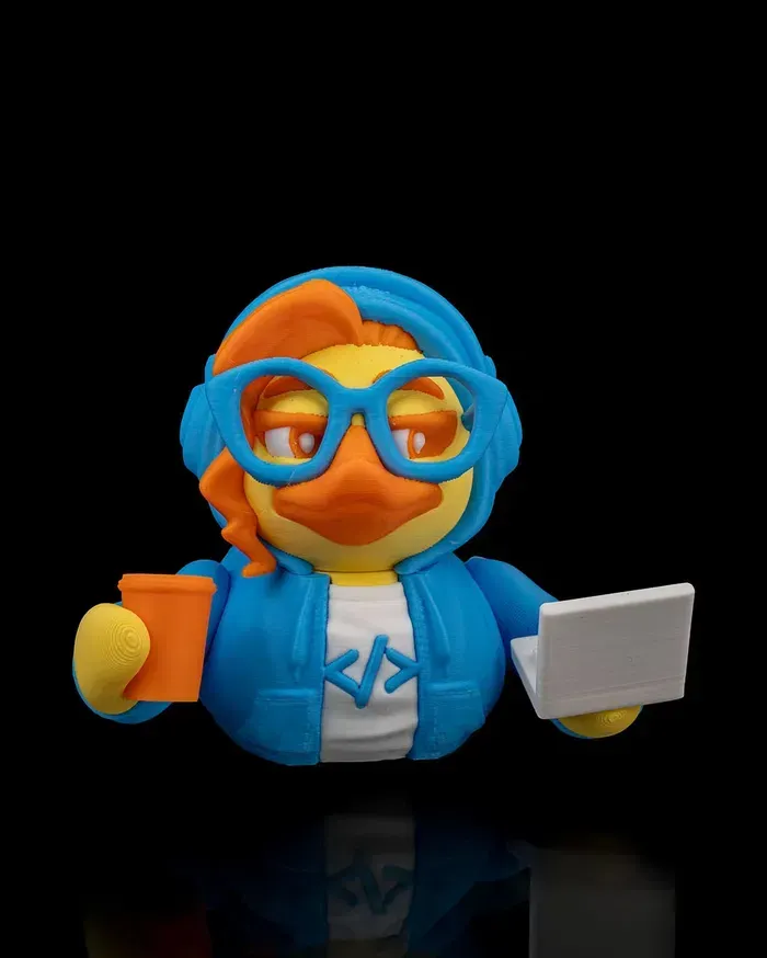 A rubber duck wearing headphones and glasses is holding a cup and a laptop.