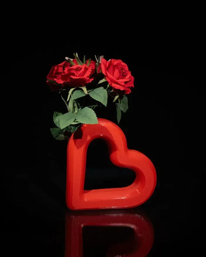 Two red roses in a red heart shaped vase on a black background.