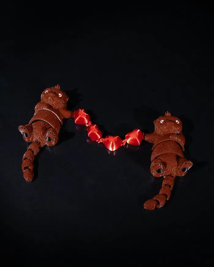 Two stuffed cats are holding a string of red hearts on a black surface.