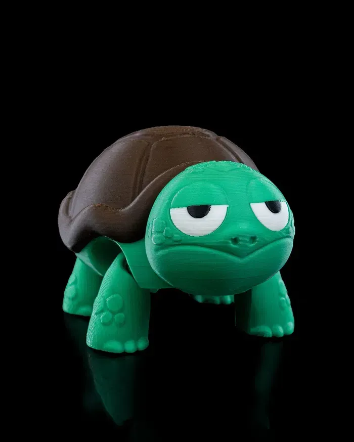 A green turtle with a brown shell is sitting on a black surface.