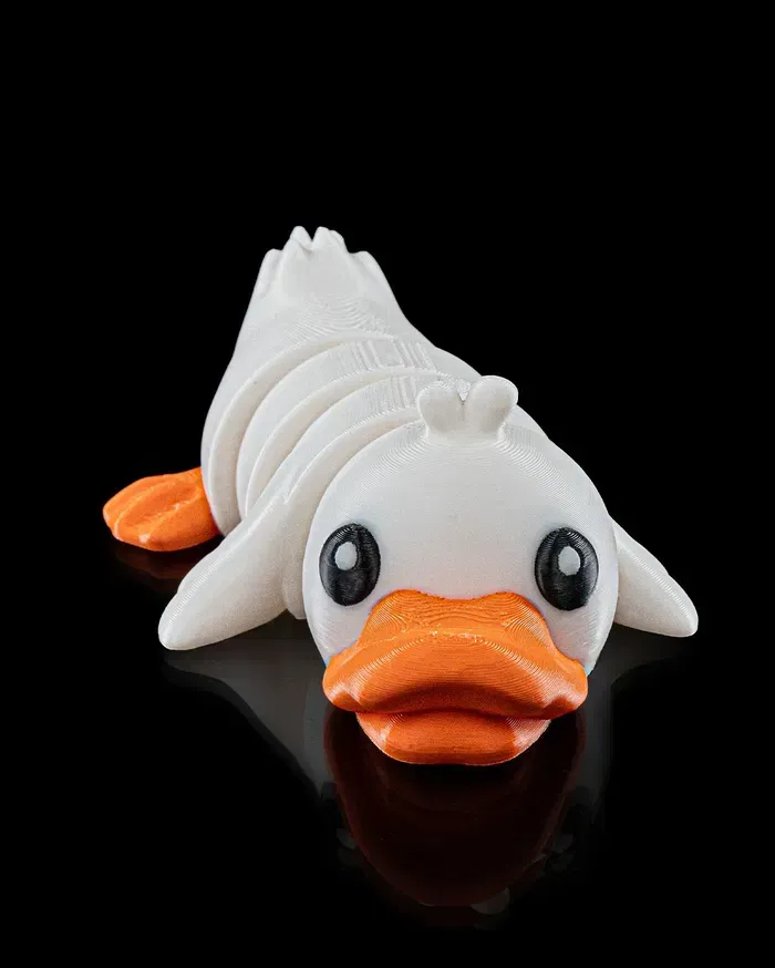 A white duck with an orange beak is laying down on a black surface.