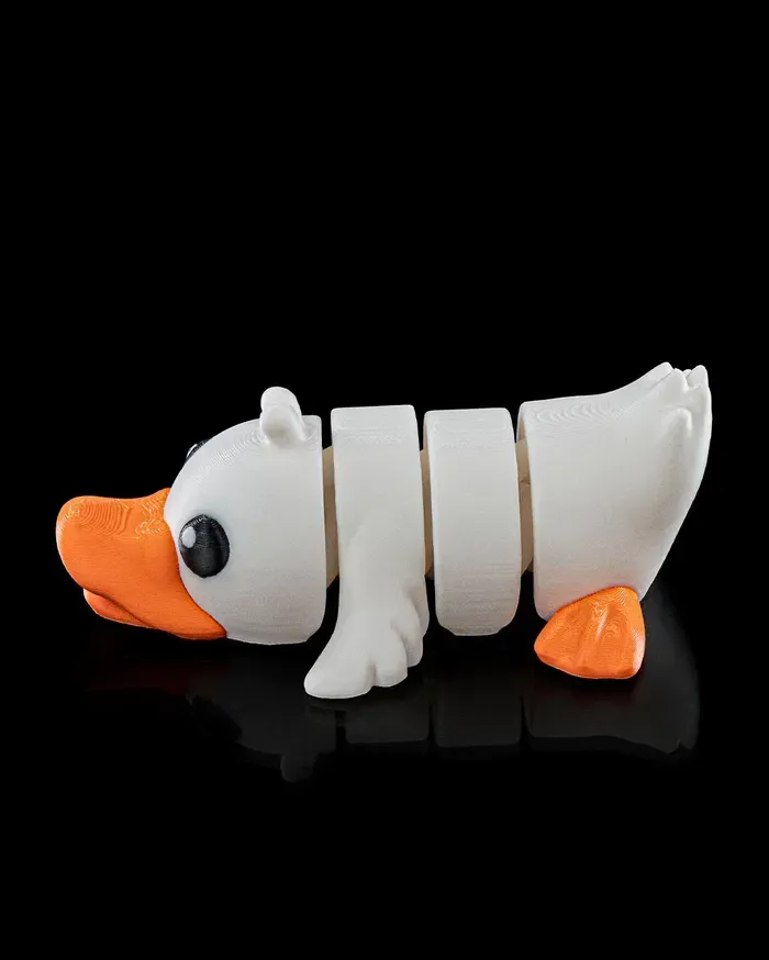 A white duck with an orange beak is laying down on a black surface.