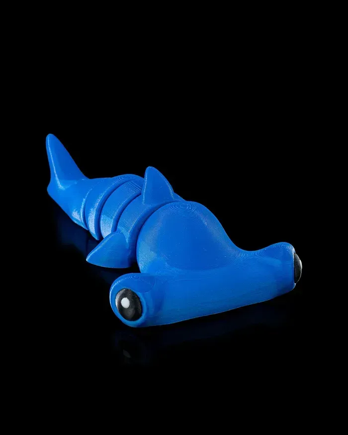 A blue hammerhead shark toy is laying on a black surface.