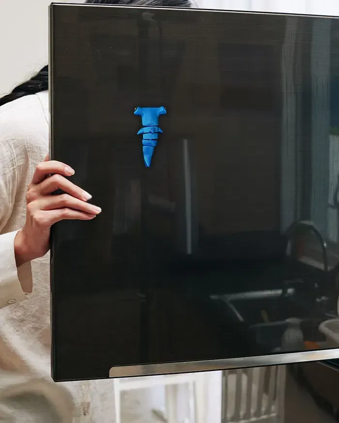 A person is holding a black laptop with a blue sticker on it.