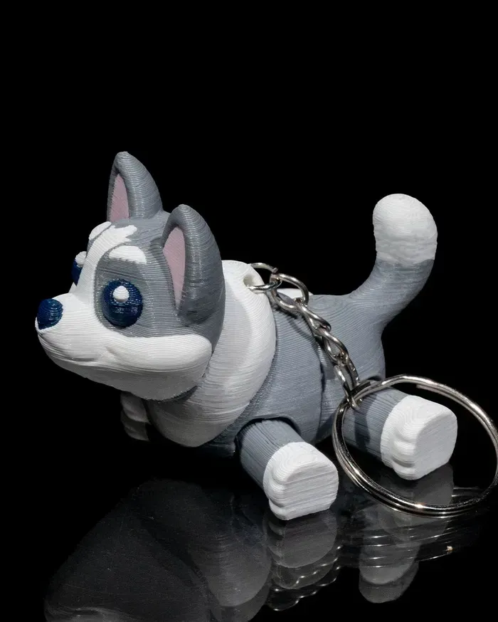 A gray and white dog keychain is laying down on a black surface.