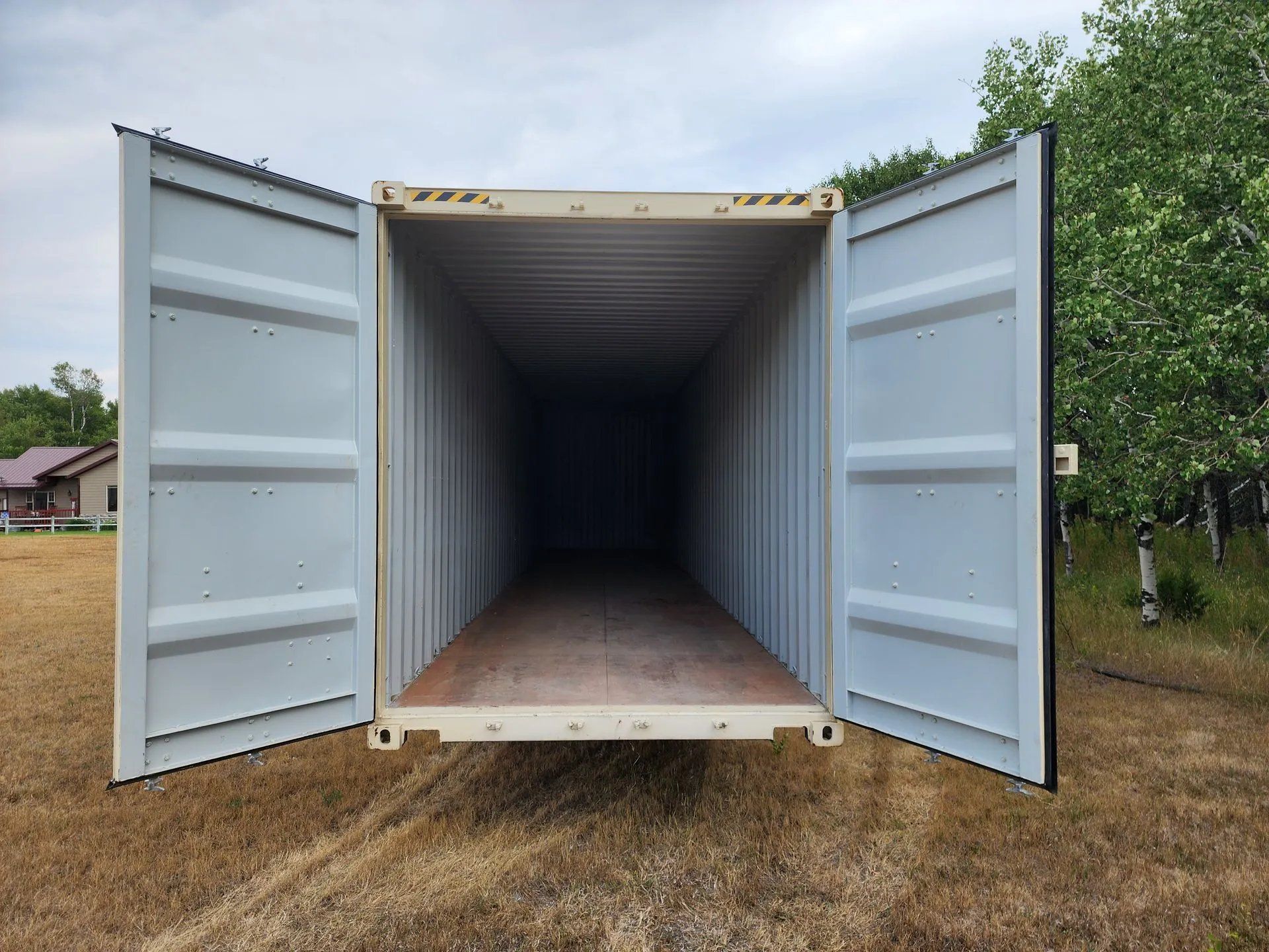 Open, empty shipping container in a field, doors ajar.