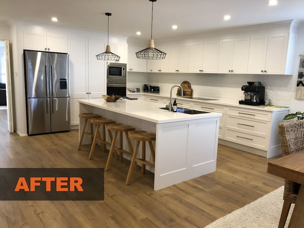 A Kitchen With White Cabinets And Stools And A Large Island In The Middle — United Kitchens and Joinery in Oak Flats, NSW