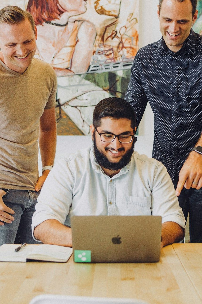 Three coworkers gathered around a laptop at a table in an office setting