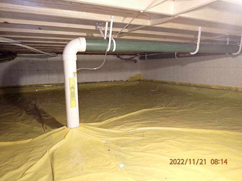 Basement crawlspace lined with yellow vapor barrier and a white PVC pipe