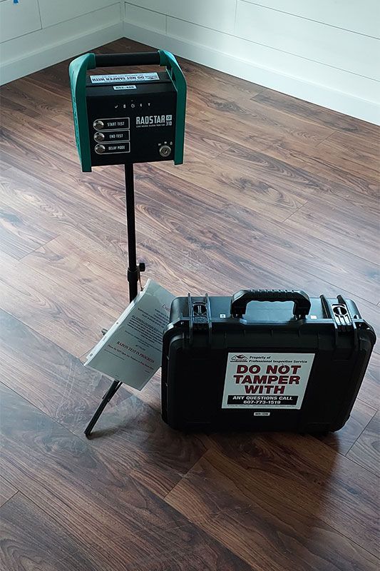 Two green-and-black electronic devices on stands in a wood-floored room; one case reads “DO NOT TAMPER.”