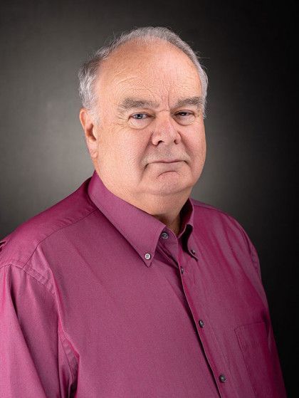 Portrait of a man in a magenta button-up shirt against a gray studio background