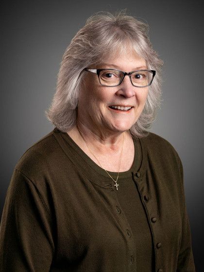 Smiling woman with glasses in an olive-green top against a gray studio background