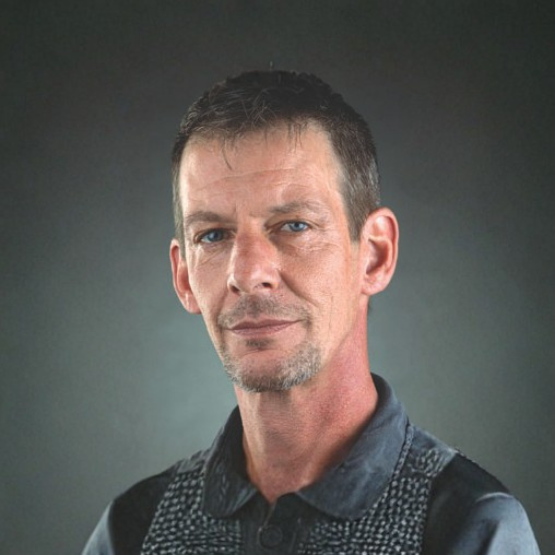 Studio portrait of a man in a dark polo shirt against a gray background