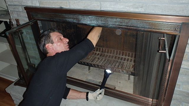 A man inspects the inside of an old fireplace with a flashlight.