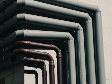 Row of dark and light industrial pipes bent along a wall, viewed in close-up.