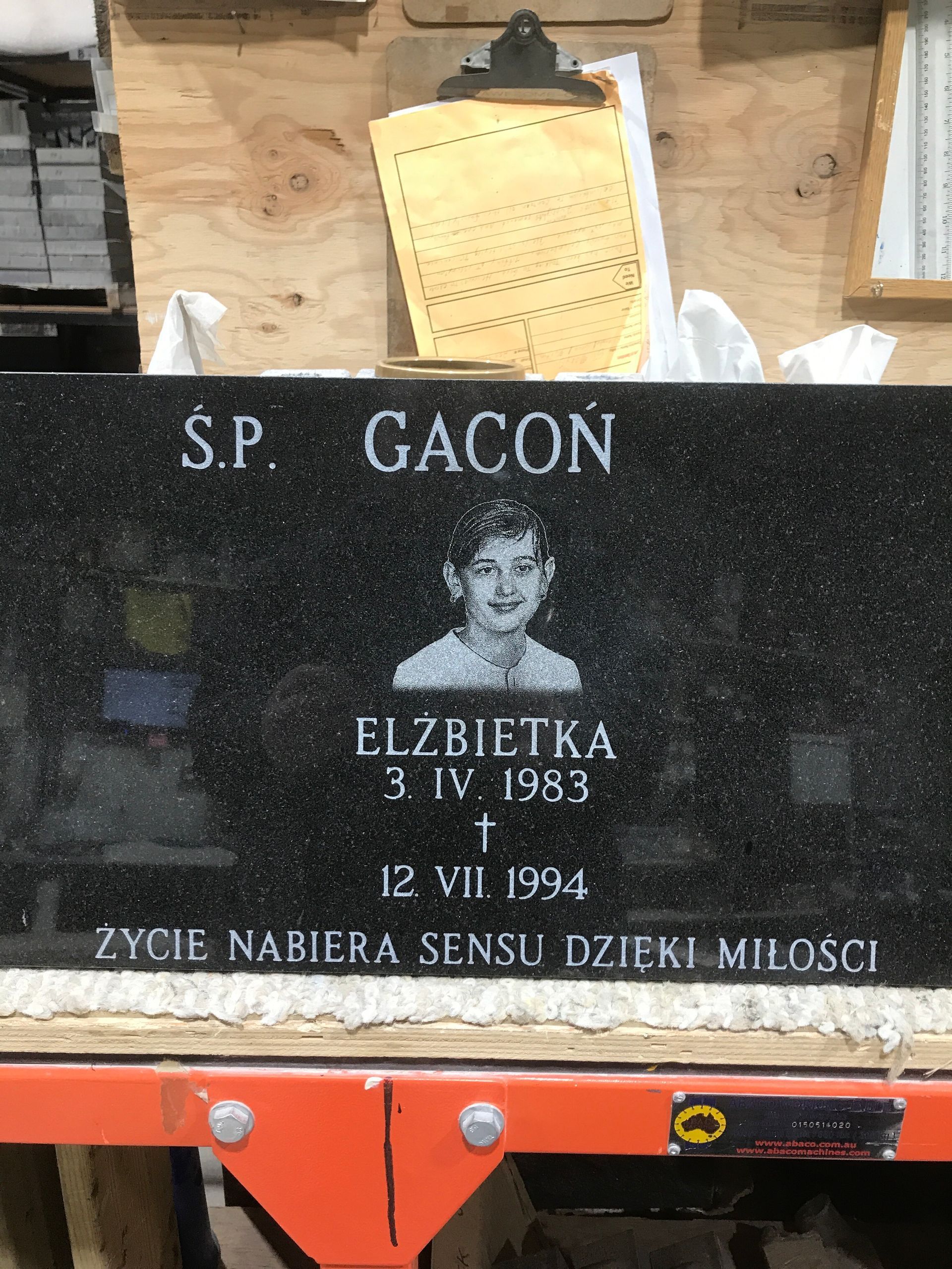 Black memorial plaque with portrait and white Polish inscription against stone wall