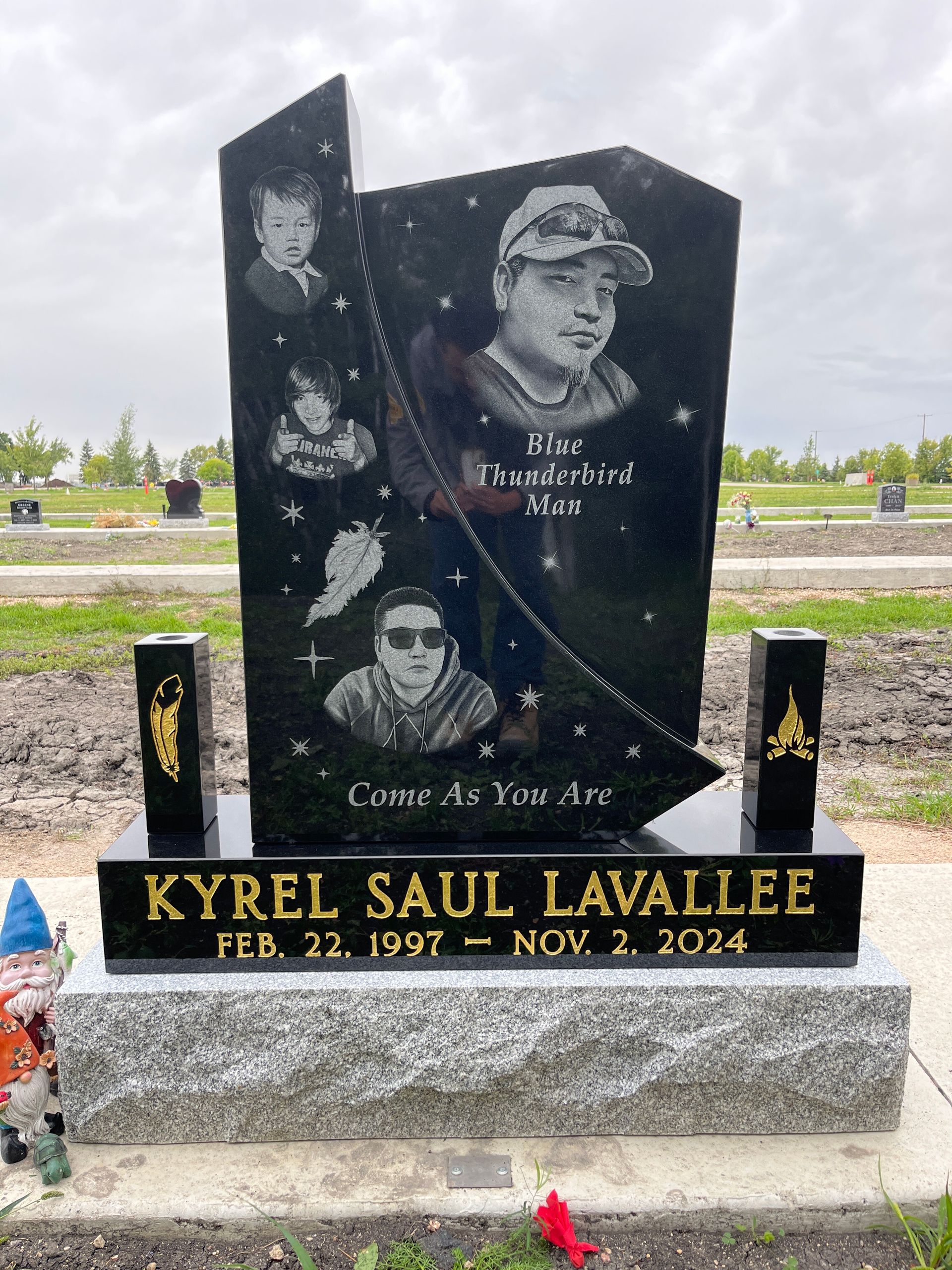 Black granite memorial headstone with engraved portraits, flowers, and the name Kyrel Saul Lavallee.