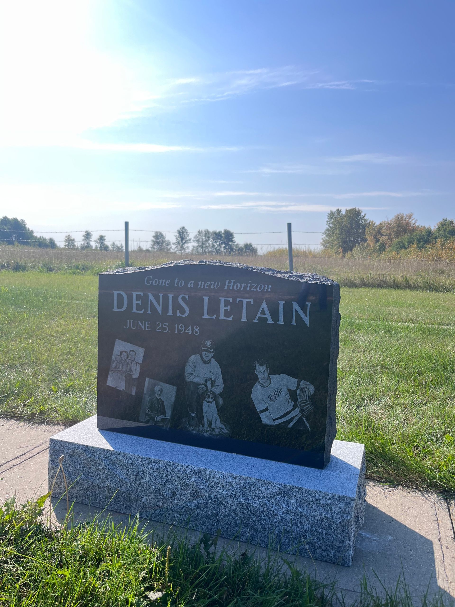 Memorial stone for Denis Letain in a sunny rural field under a blue sky