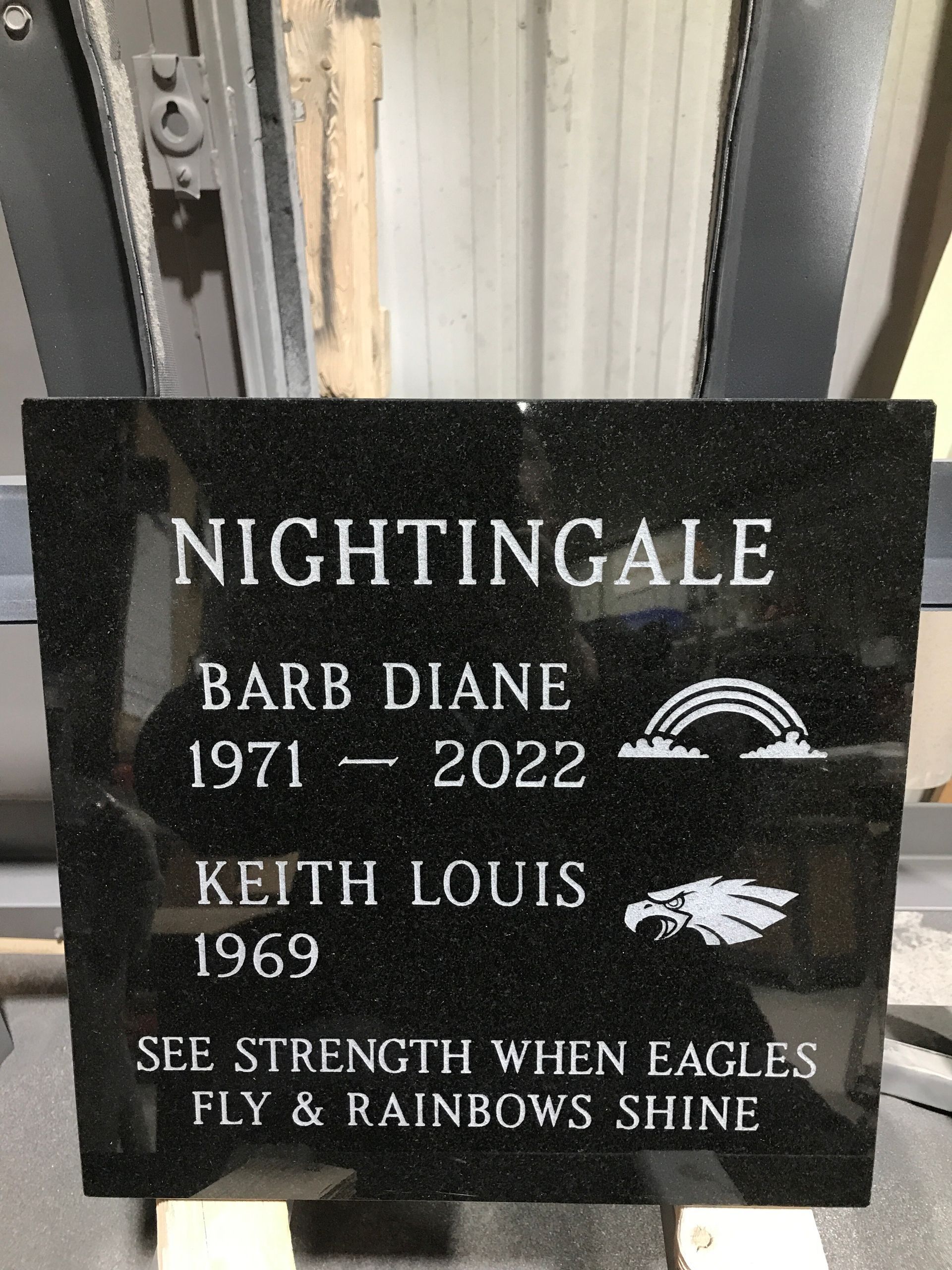 Black memorial plaque reading “NIGHTINGALE” with names Barb Diane and Keith Louis, plus a rainbow and eagle icon.