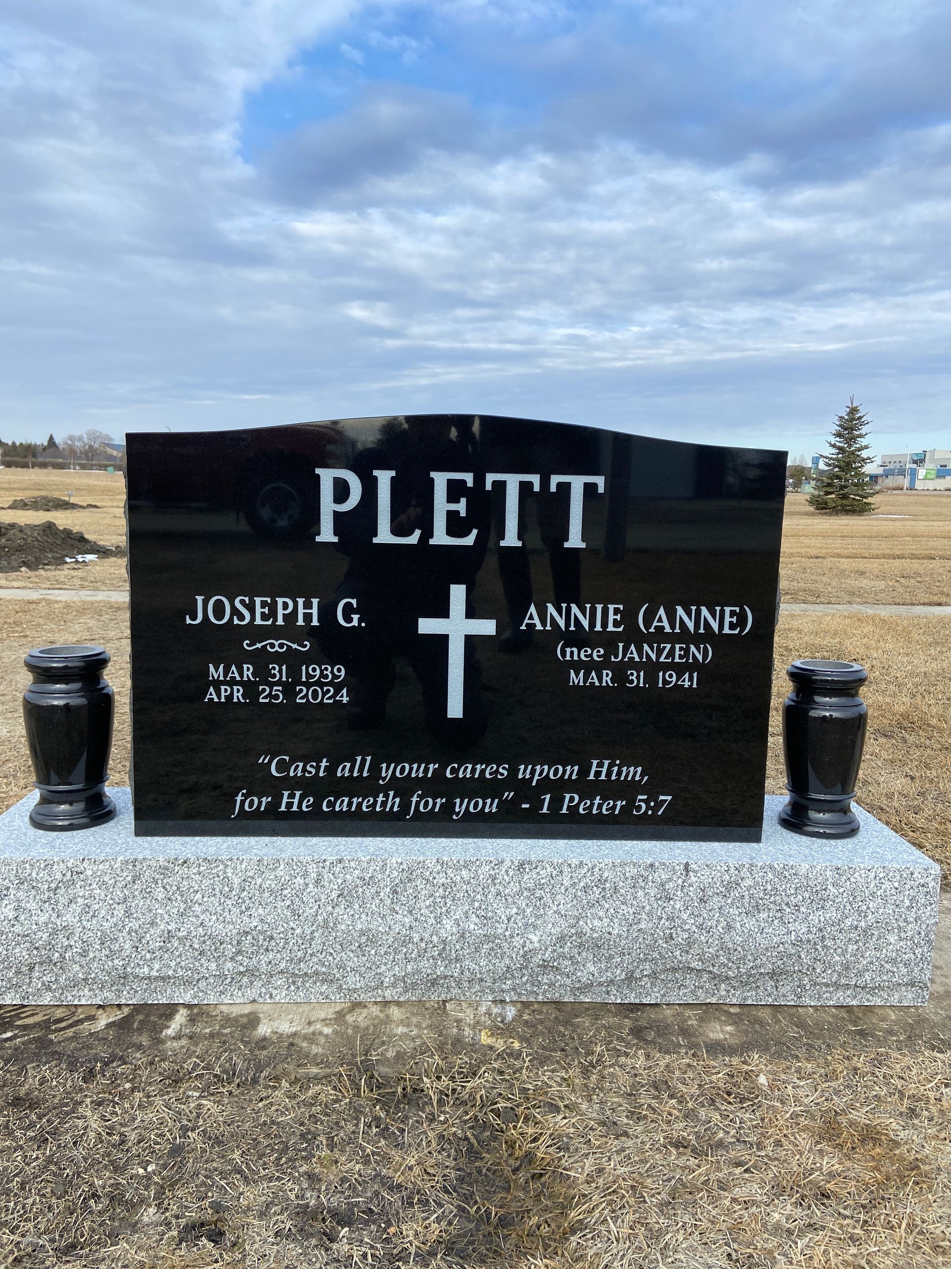 Black granite Plett family gravestone in a cemetery under a cloudy sky.