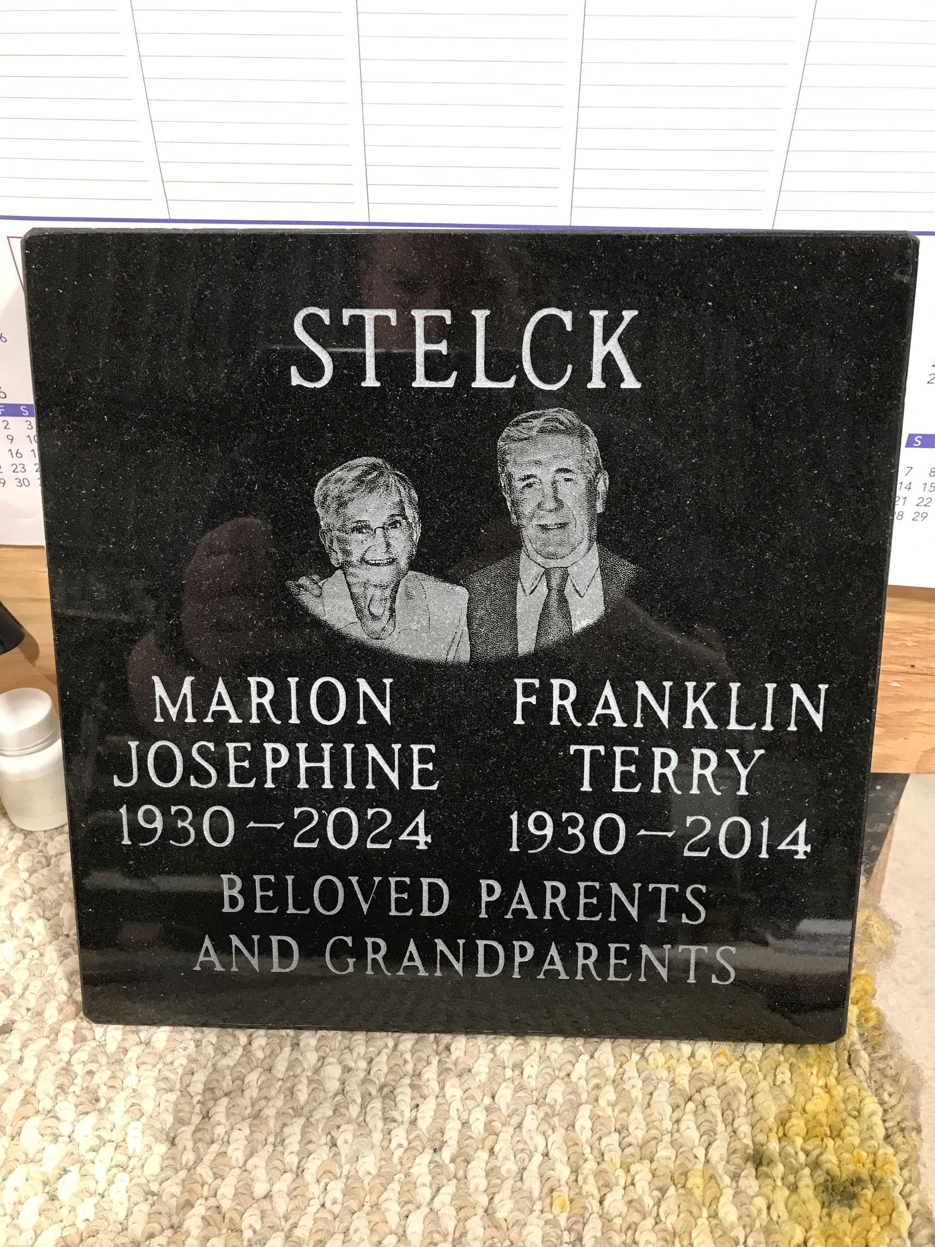 Black memorial gravestone with etched portraits and the names Marion Josephine and Franklin Terry Stelck, 1930–2024 and 1930–2014