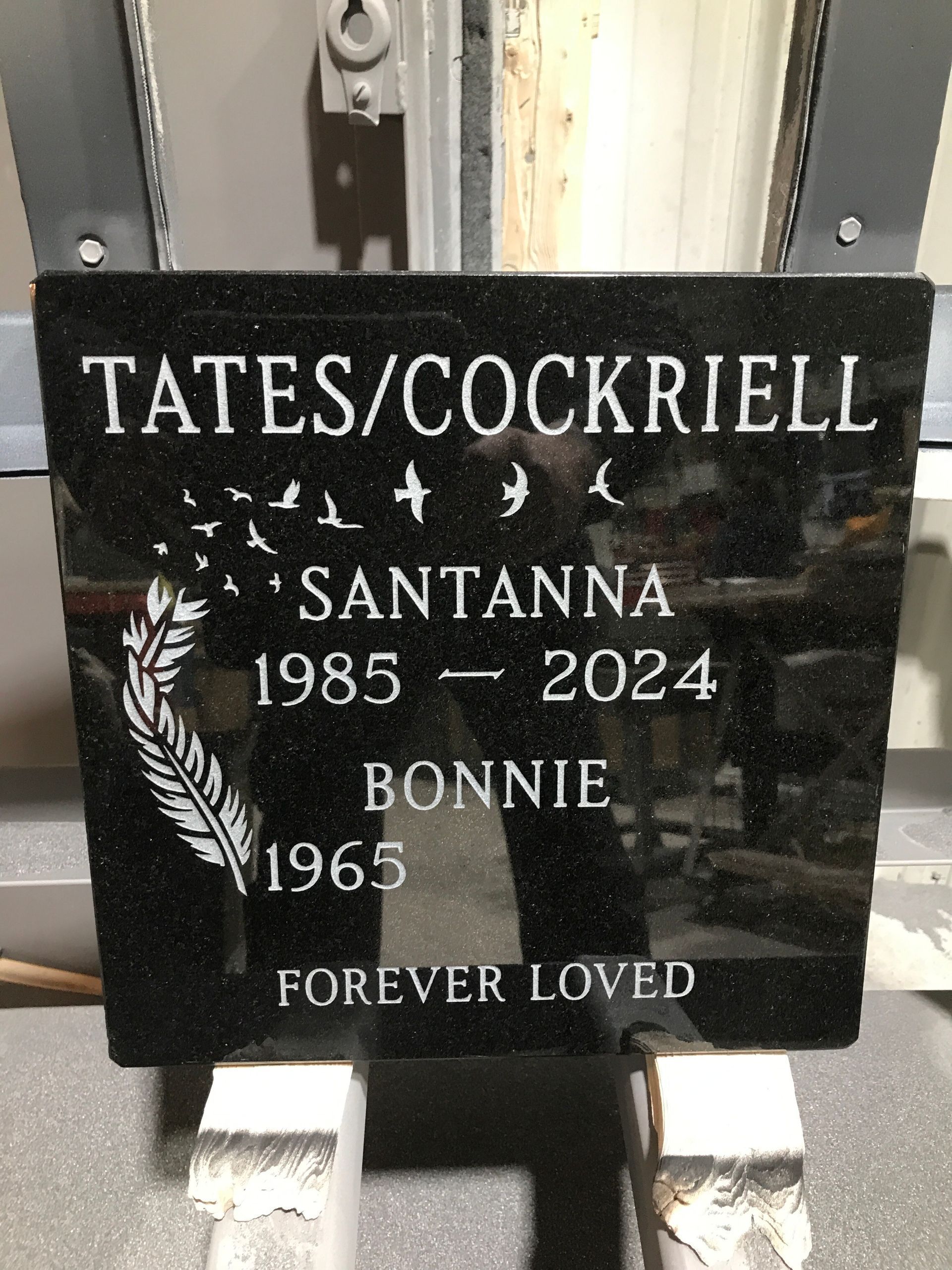 Black memorial plaque reading “Tates/Cockriell,” “Santanna 1985–2024,” “Bonnie 1965,” “Forever loved.”