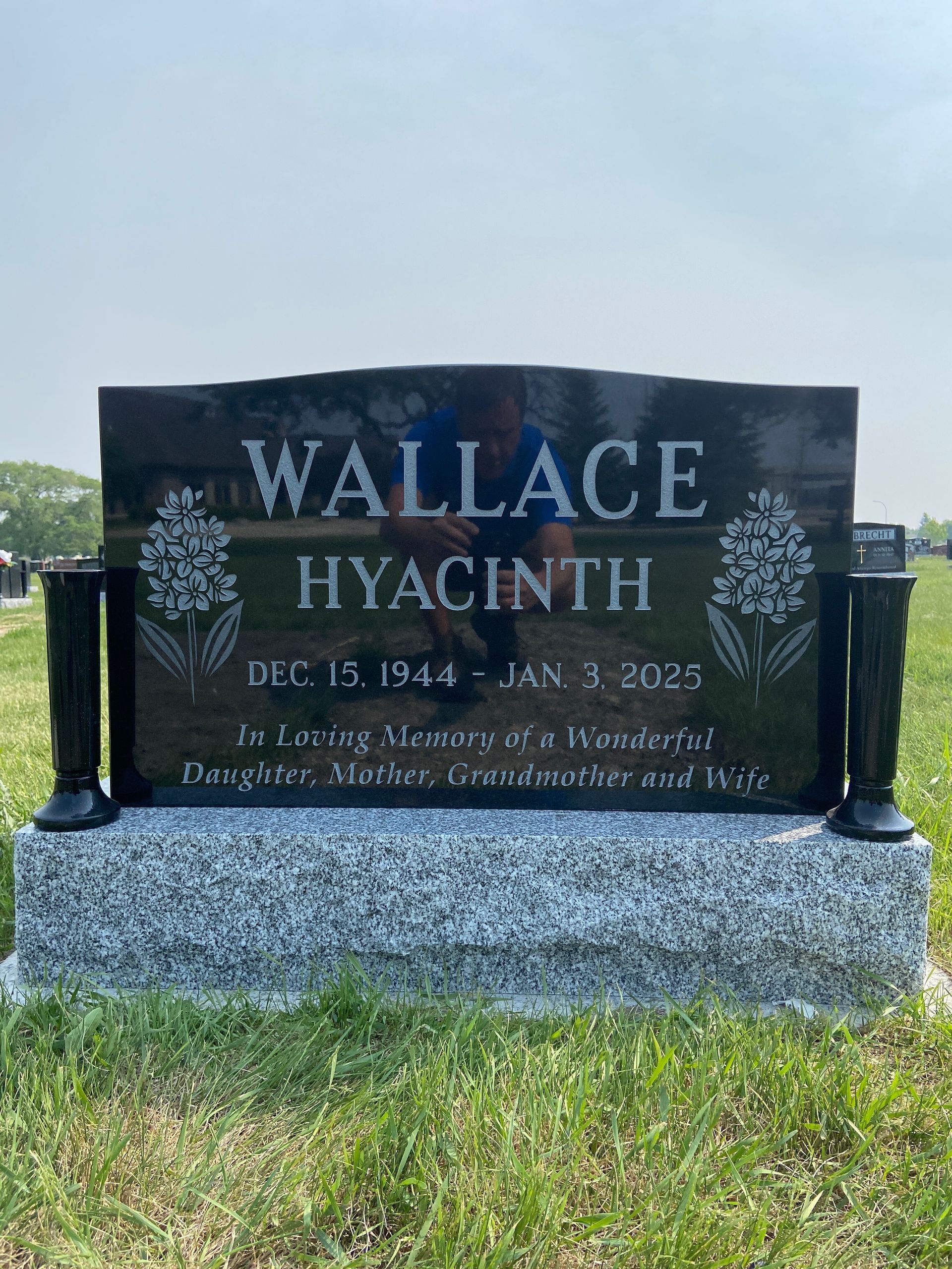 Black granite gravestone reading “WALLACE HYACINTH” in a grassy cemetery.