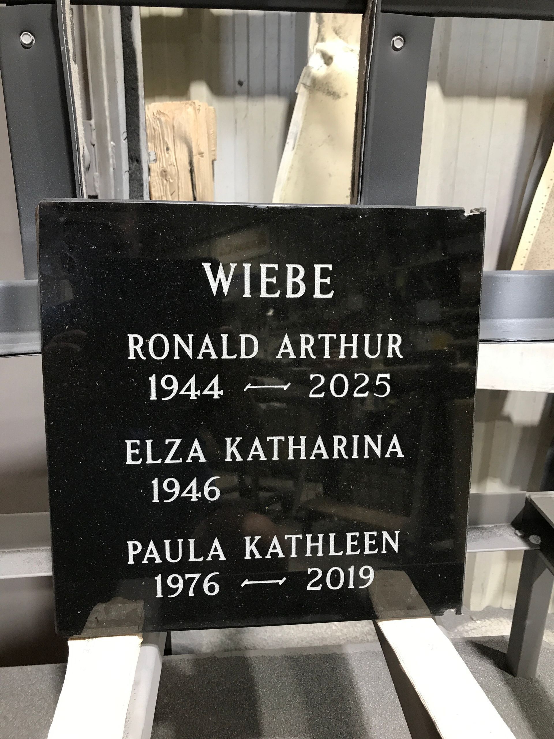 Black granite gravestone engraved with the Wiebe family names and dates in a cemetery.