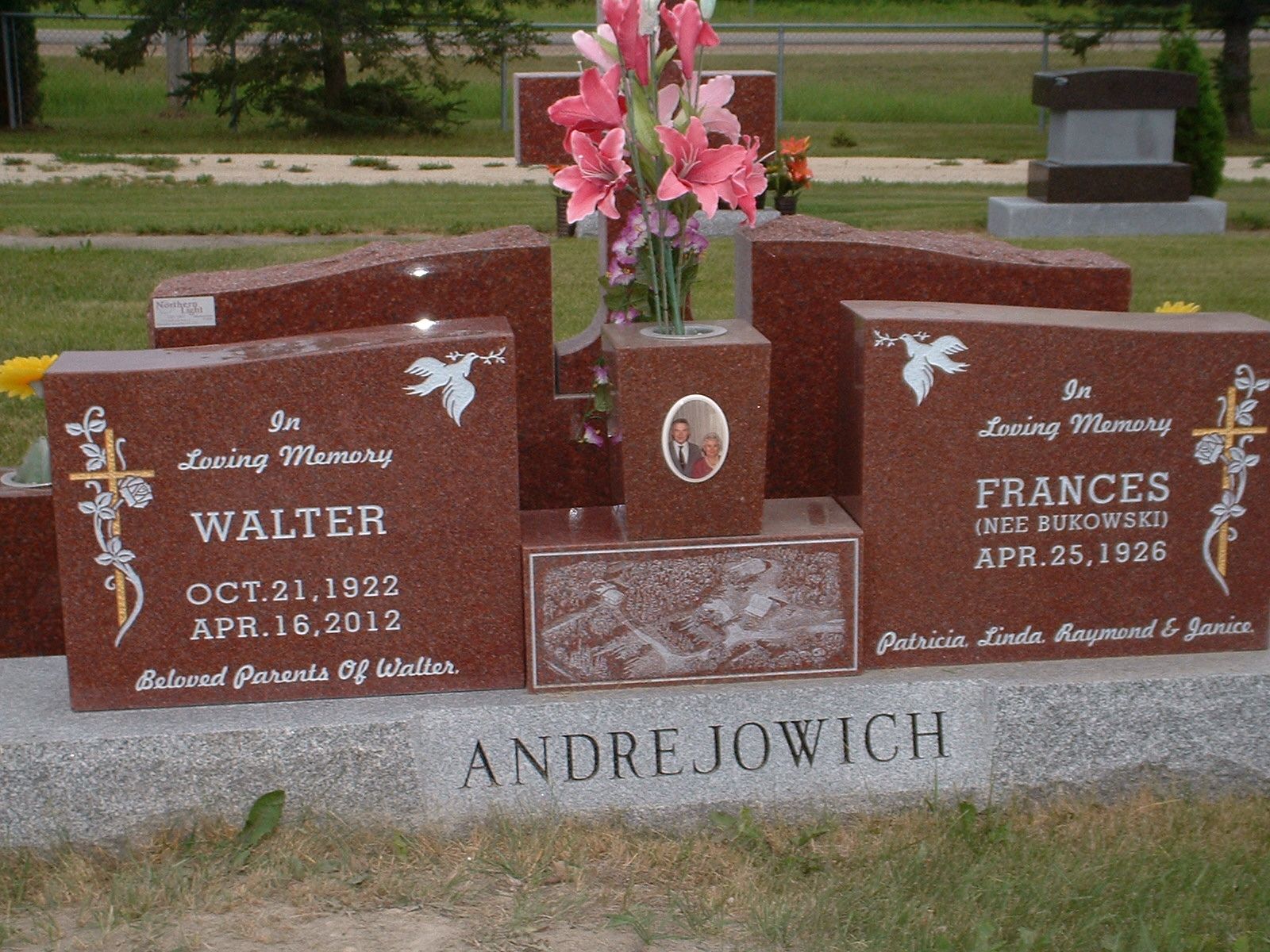 Gravestone with two red memorial markers and pink flowers at Andrzejowich cemetery plot