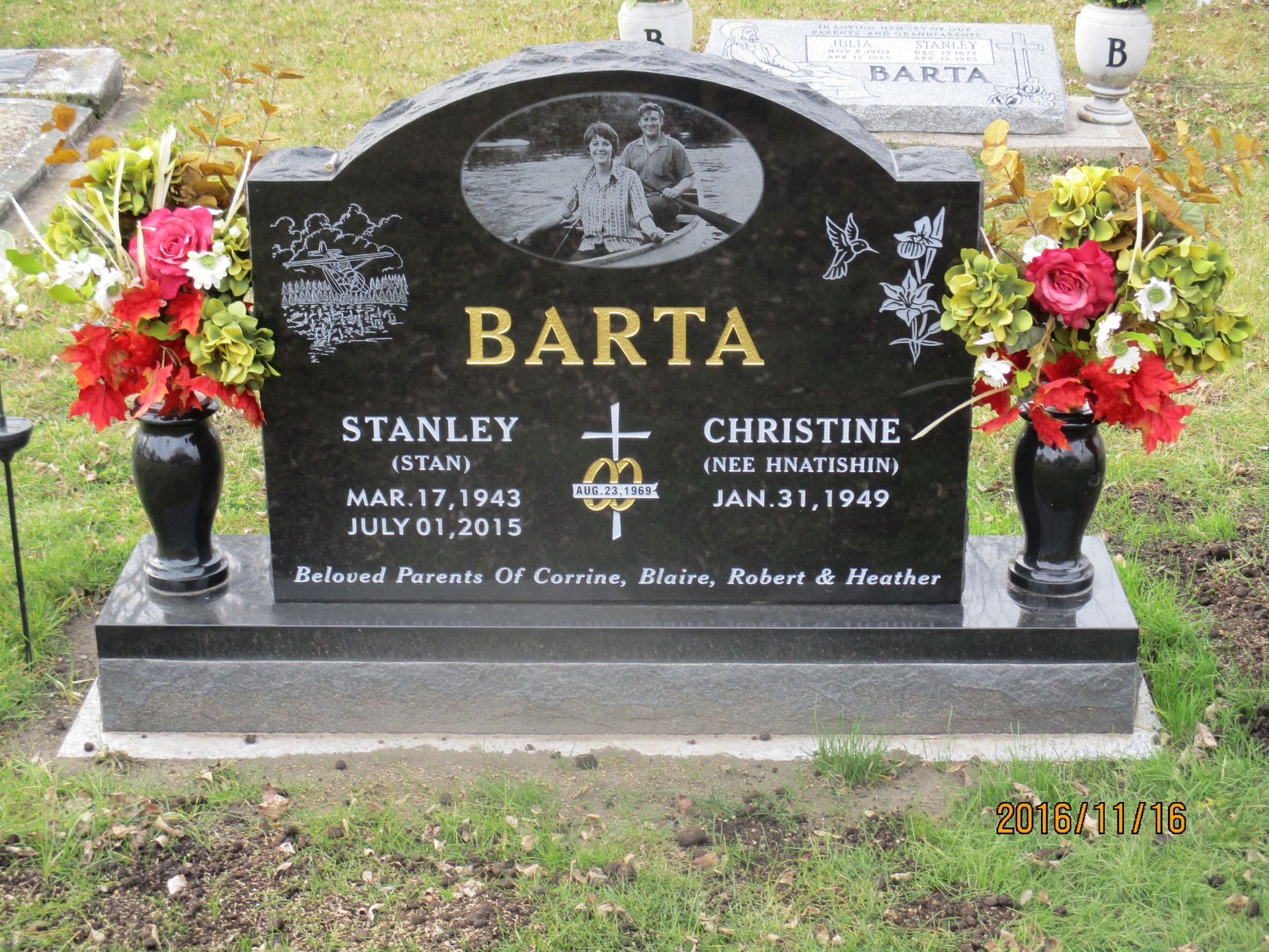 Barta family gravestone with black headstone and red flowers in a cemetery
