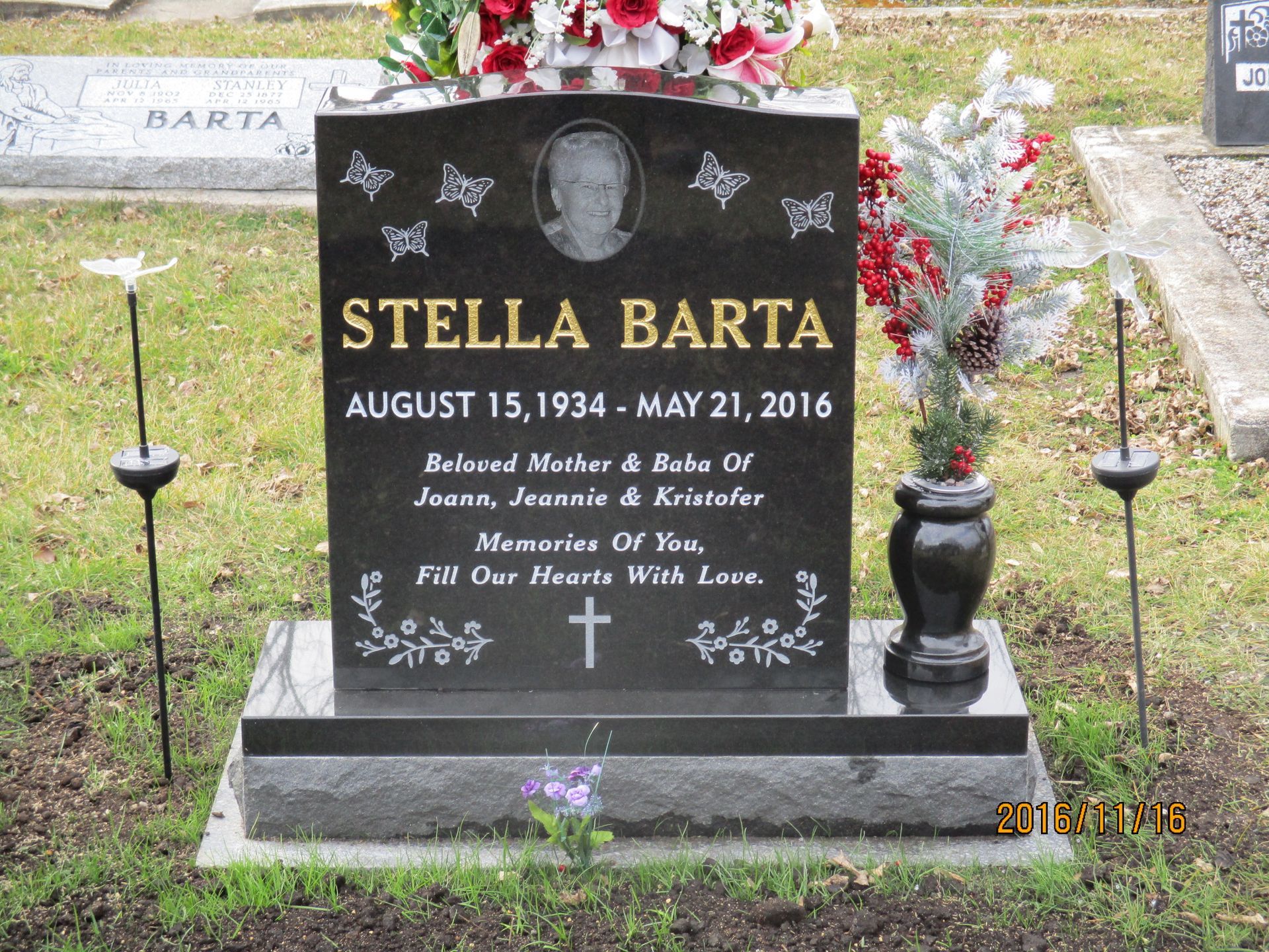 Black granite memorial gravestone with flowers and a vase, engraved “Stella Barta.”