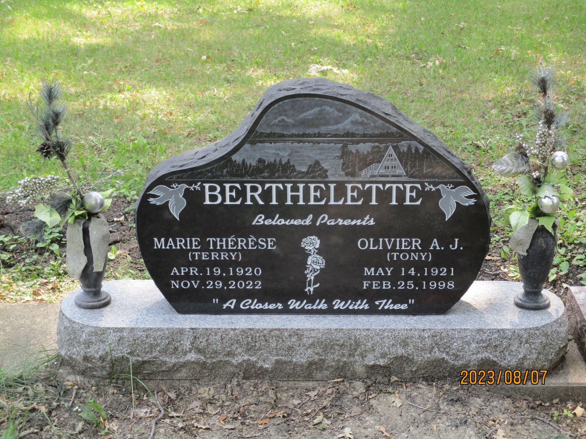 Black granite Berthelette family gravestone with flower vases in a grassy cemetery