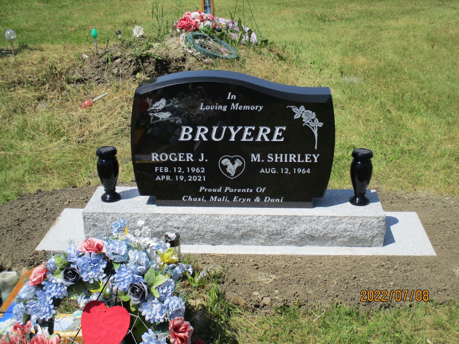 Black granite grave marker with flowers on a grassy cemetery plot
